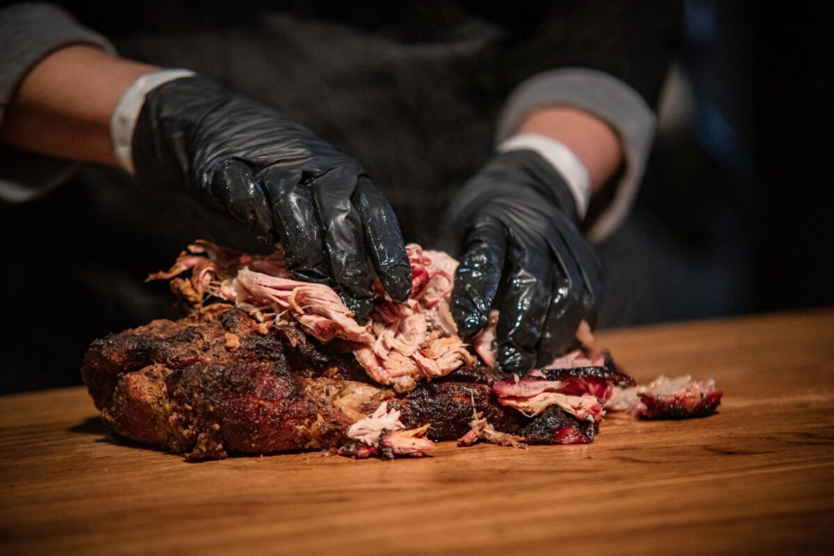 Pulled Pork wird mit Handschuhen auf dem Brett gezupft