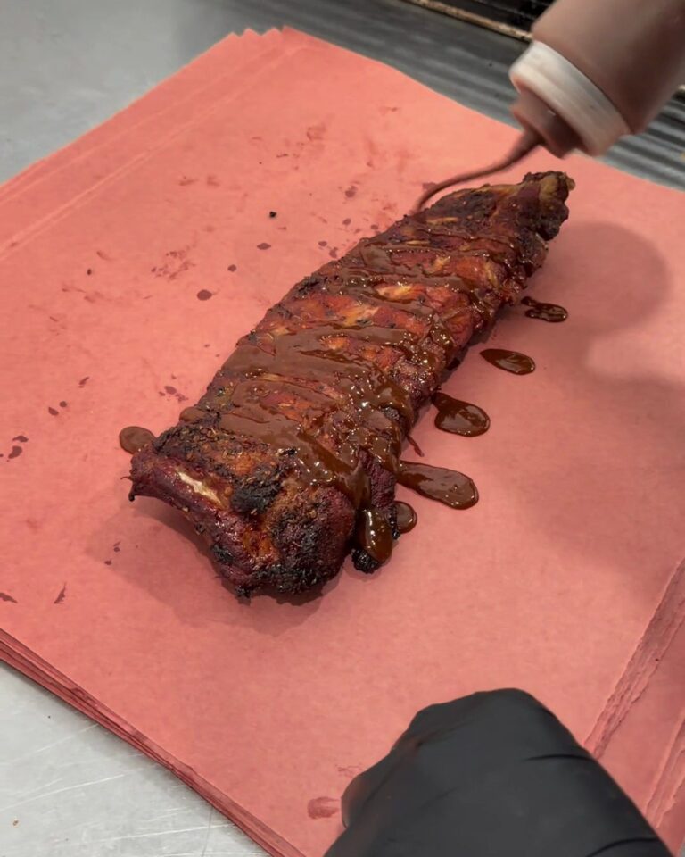 Geräucherte Ribs auf Butcher Paper, darüber läuft BBQ-Sauce aus der Flasche