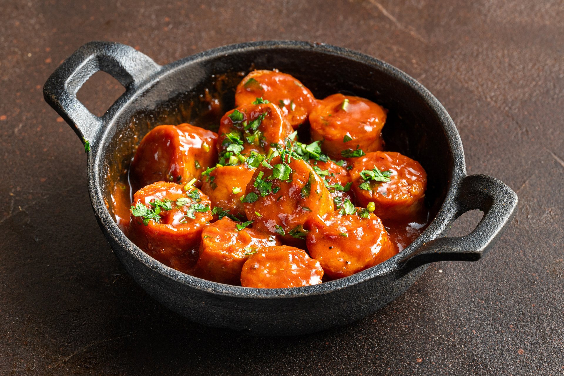 Texas Hot Links in Scheiben, in Tomatensauce mit frischen Kräutern in einer Gusseisenpfanne